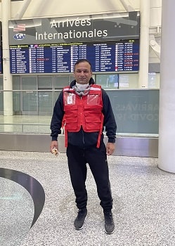 A man in a Canadian Red Cross vest standing in Arrivals section of an airport