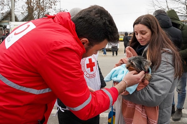 A member of the Turkish Red Crescent Society talking with a woman holding a small dog.