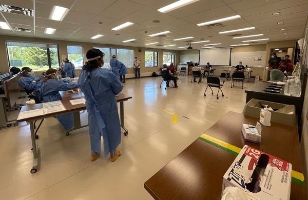 A room full of people in PPE with tables and chairs set up