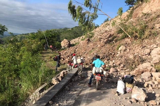 People on bikes, mopeds, and on foot going around a landslide which obstructed a road.
