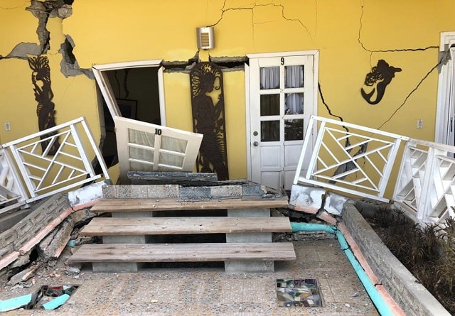 A yellow house cracked and doors falling from its frame
