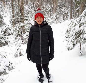 A woman standing in a snow-covered forest, on a snowy path.