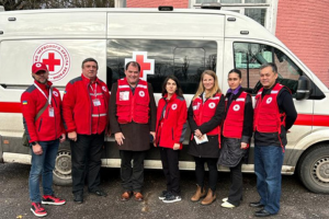 A group of Red Cross personnel pose for a photo in front of a Mobile Health Unit.