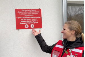 A woman smiles, while pointing to a plaque on the outside of a refurbishment site.