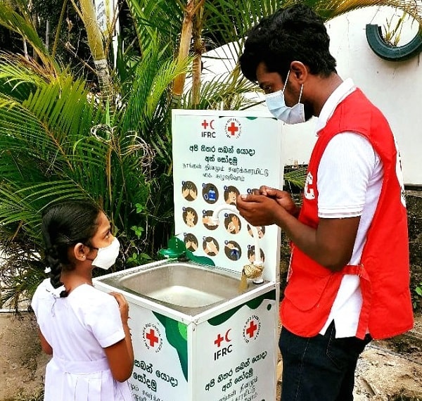 A member of Sri Lanka Red Crescent Society with a young girl in front of a