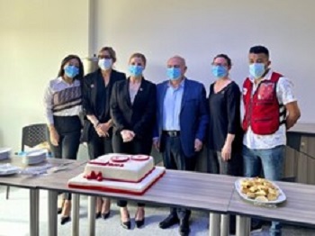 A group of people wearing masks standing together behind a table with a cake on it.
