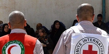 Back view of a man wearing a red vest with Red Crescent beside a man with a white ICRC vest.