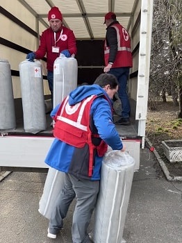 Men in Red Cross vest unloading bags of supplies from a large white truck