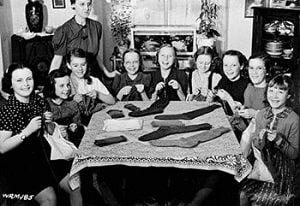 An archival photo of a group of women sitting around a table knitting