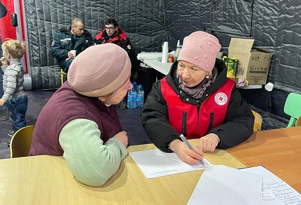 A Red Cross team member sitting at a table with a woman writing notes