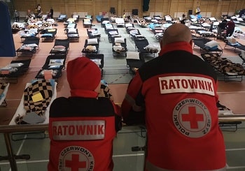 Two Red Cross members viewing a room set up with cots for those fleeing Ukraine