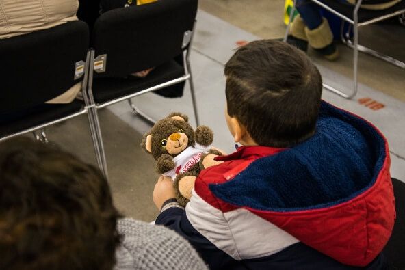 A boy sitting in a chair holding a Red Cross teddy bear