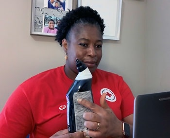 A woman with a bottle of household cleaner pointing to the fine print on the back of the bottle to someone on the laptop
