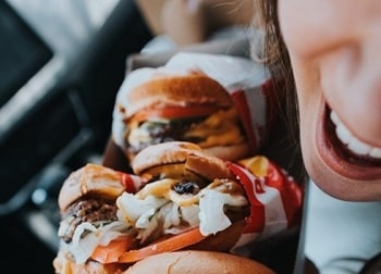 An open smiling mouth by a row of small burgers lined on a plate
