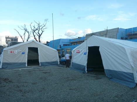 The field hospital is set up in a series of tents, in front of the damaged local hospital.