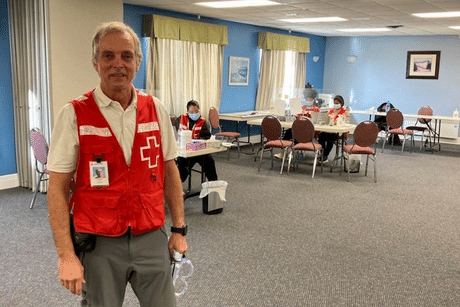 Denis Lessard wearing a Red Cross vest and smiling to the camera at a reception center