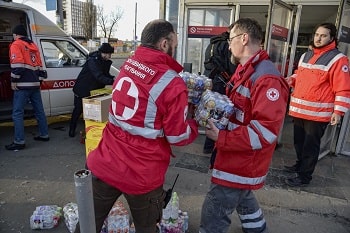 People in Red Cross jackets carrying cases of water bottles, distributing food to people sheltered at the metro stations during the shelling.