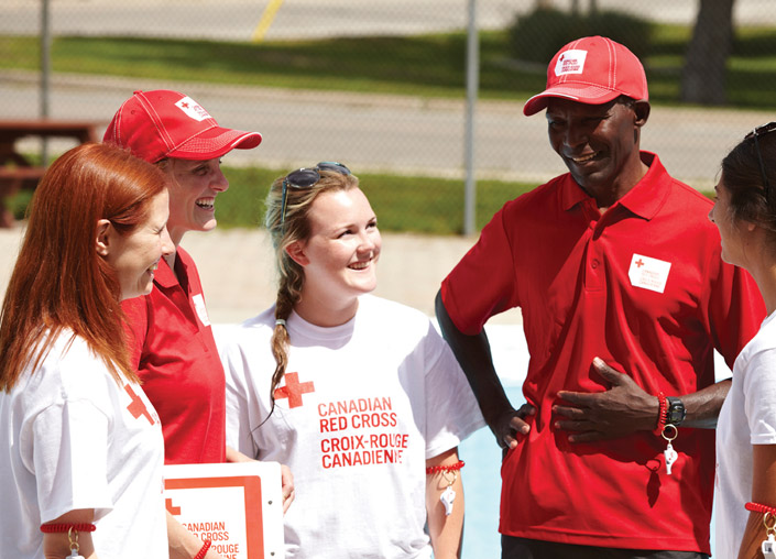 A group of Red Cross volunteers dress in Red Cross clothing are standing casually in a group having a conversation.