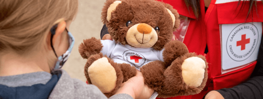 A Red Cross volunteer presents a teddy bear to a small child to provide comfort.
