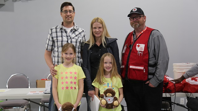 Family with two young kids stands next to a Canadian Red Cross man at an Alberta fire relief center.