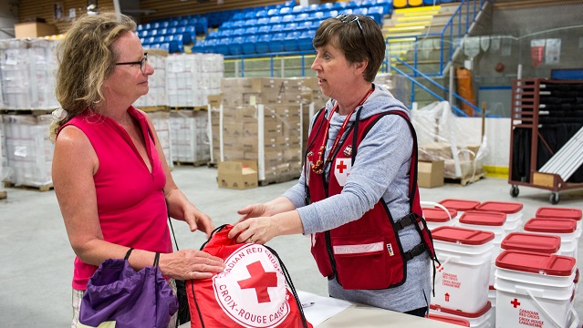 A Red Cross worker is handing a filled bag that has a Red Cross logo on it to someone. 