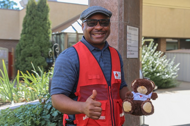 A Red Cross volunteer holding a teddy giving the thumbs up.