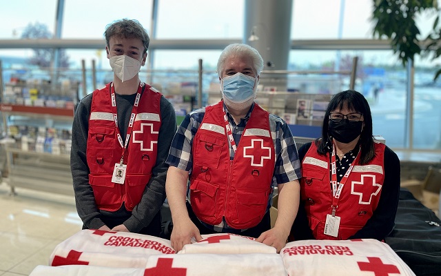 Three Red Cross volunteers wearing red vests and masks. 