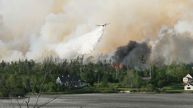 A large plane flies overhead to put out a large forest fire.