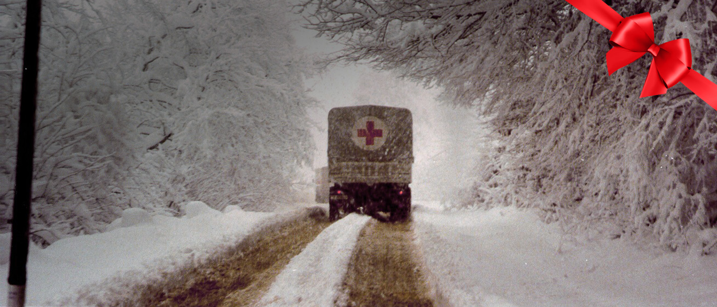 A Red Cross truck drives on a snowy road.