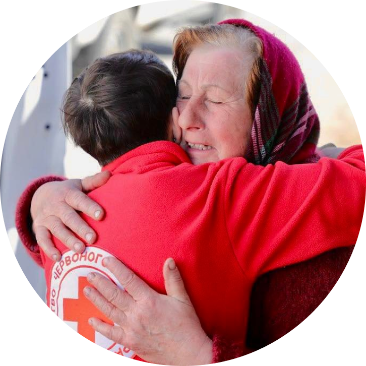 A Red Cross volunteer embraces an older woman in a warm hug.