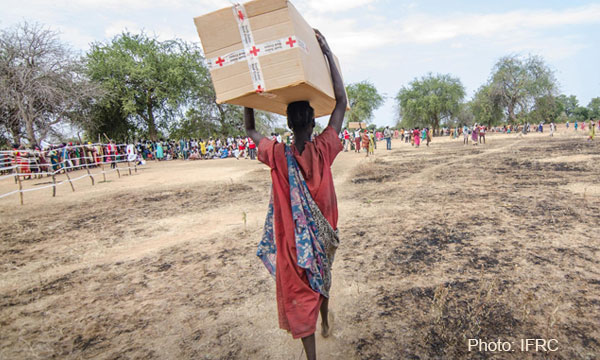 A person carries a large box full of Red Cross aid above their head, photo by IFRC..