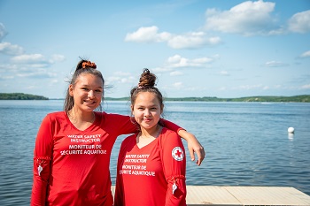 Two young female Red Cross lifeguards standing in front of a beach