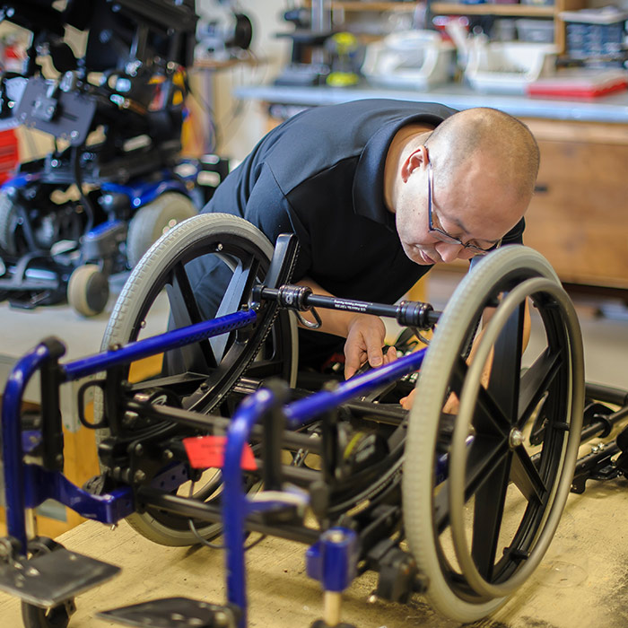 A man is working to refurbish a wheelchair in a Health Equipment Workshop.