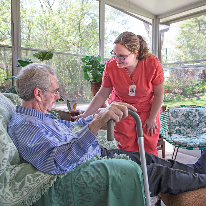 A Registered Nurse provides care to an elderly man sitting comfortably in a chair.