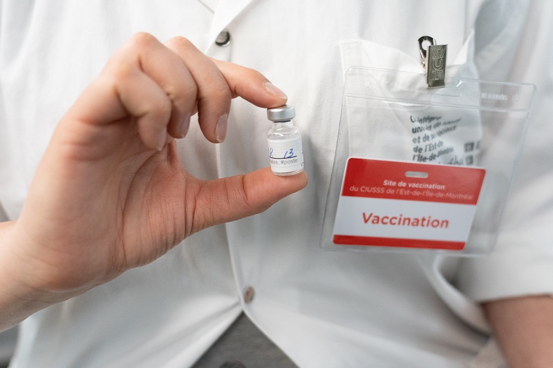 Person in white lab coat holding small vial