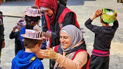 Red Crescent person puts a fun hat on a child