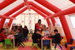 Red Crescent volunteer watching kids play in a colourful tent