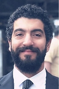 Man with dark curly hair, full beard and dark suit