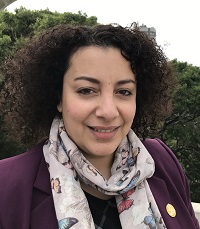 Woman with dark curly hair, butterfly scarf, and purple suit jacket