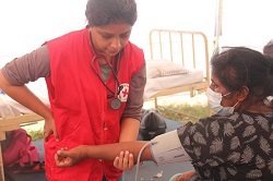 Woman in Red Cross vest taking the blood pressure of another woman