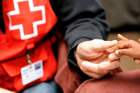 A person in a Red Cross vest holding hands with a child