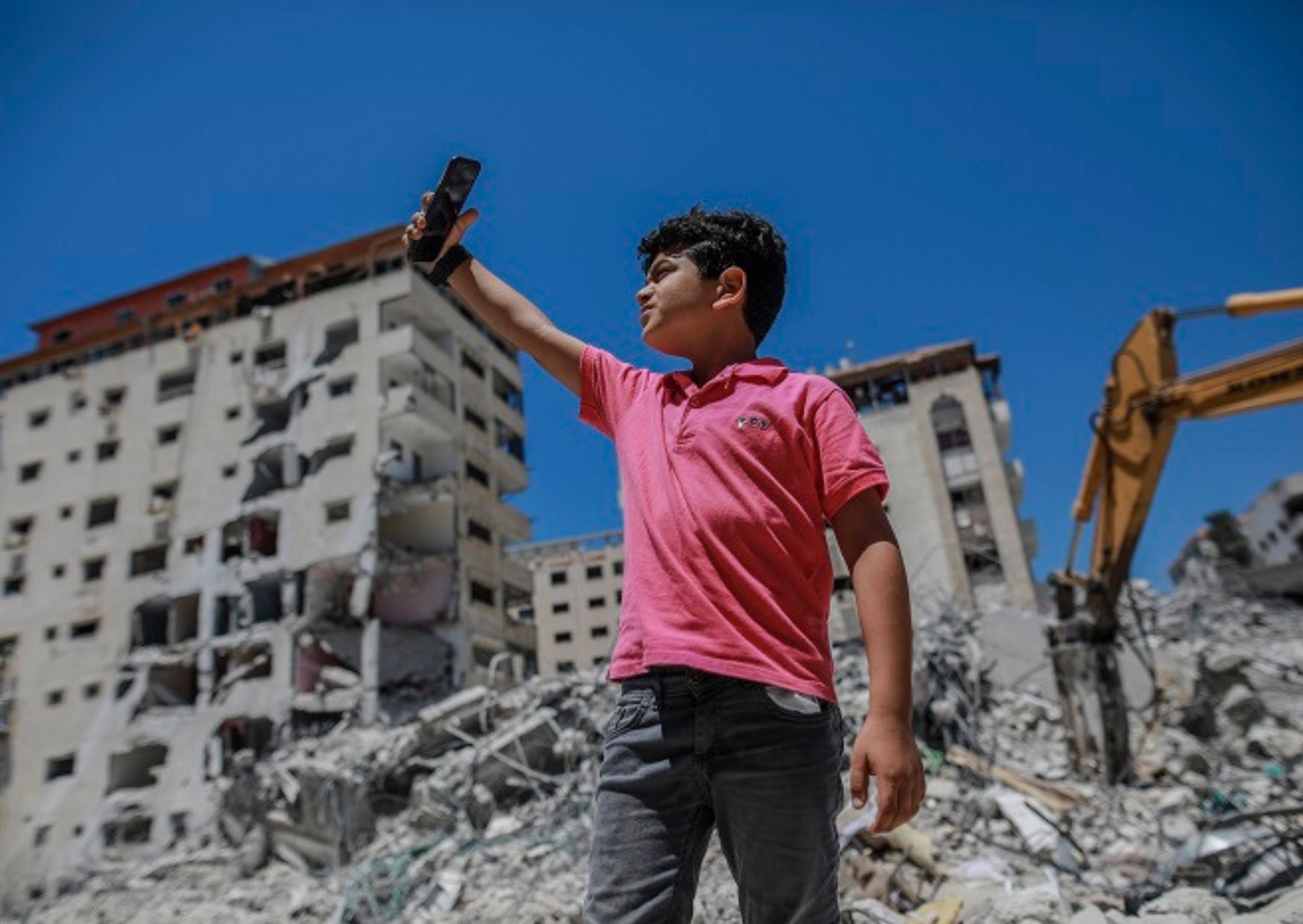 a child holding a phone in front of a destroyed building.