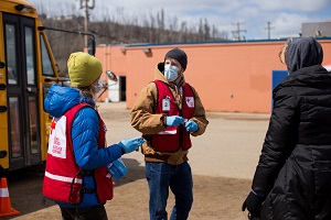 Two Canadian Red Cross employees wearing masks talking to a woman