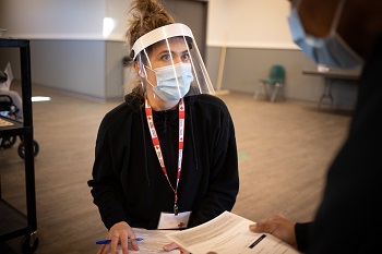 A Canadian Red Cross employee wearing a mask and a face shield talking to another employee