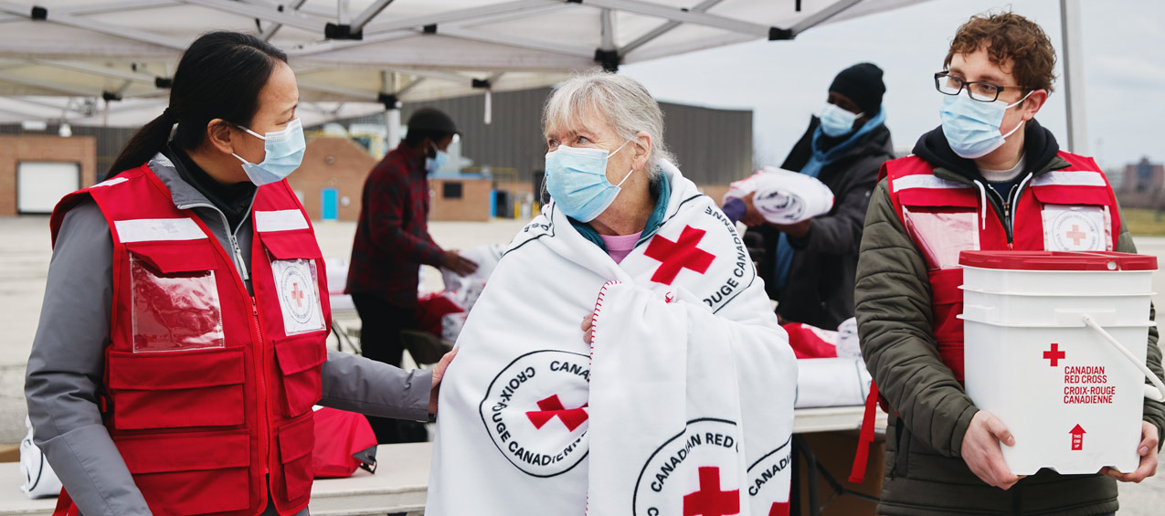 Deux volontaires de la Croix-Rouge viennent en aide à une femme âgée.