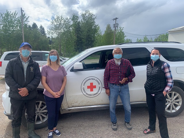 Four people wearing masks in front of a Red Cross automobile