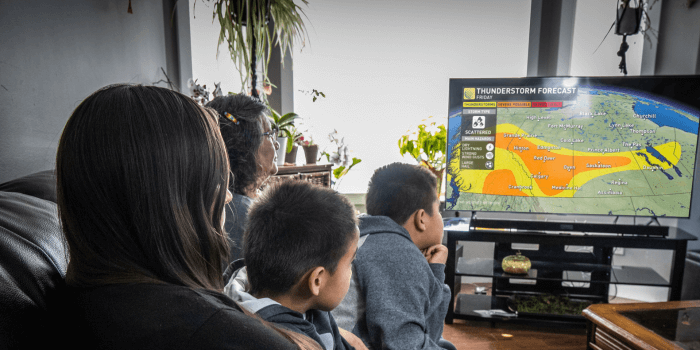 A family of four watching the weather channel announcing a thunderstorm
