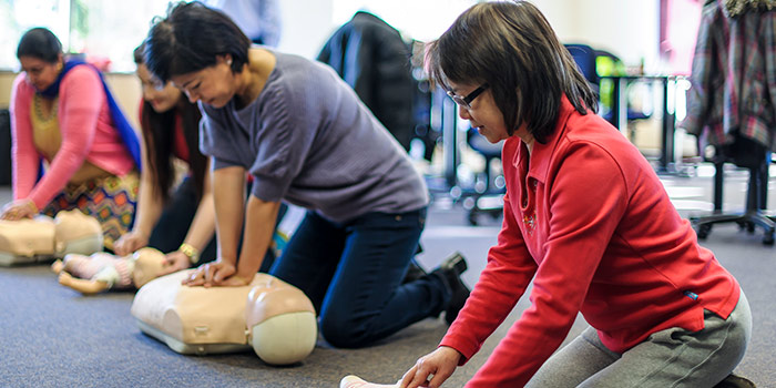 Four women are on their knees, administering CPR to dummies.