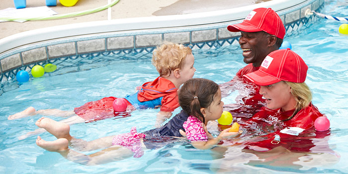 Two Red Cross lifeguards assist two toddlers in the pool.