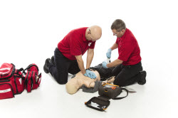 Two men in red shirts preforming CPR to a practice dummy.